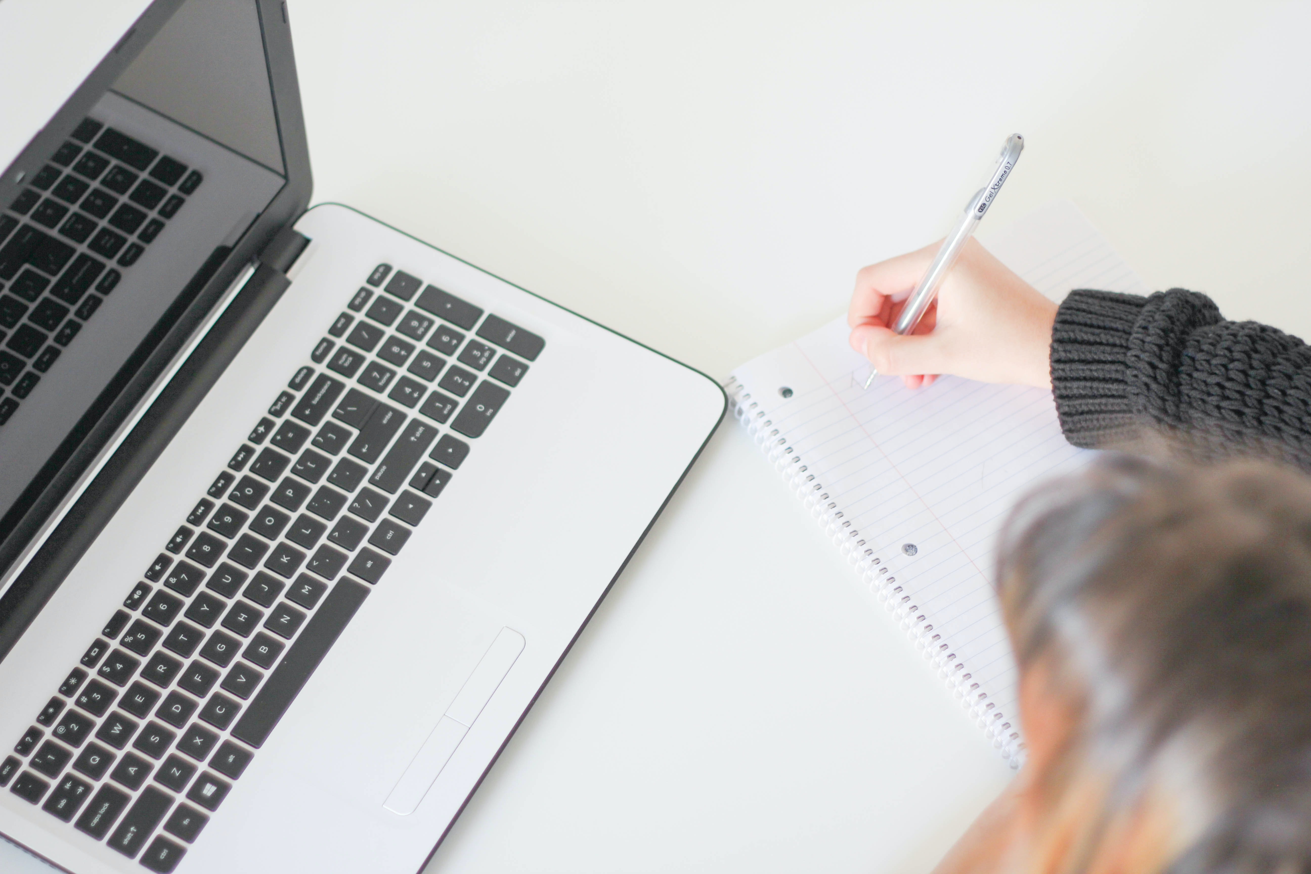 Person looking at a computer and taking notes on paper with a pen