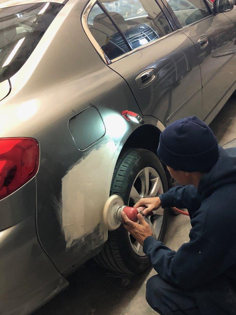 Apprentice polishing a repair to car fender